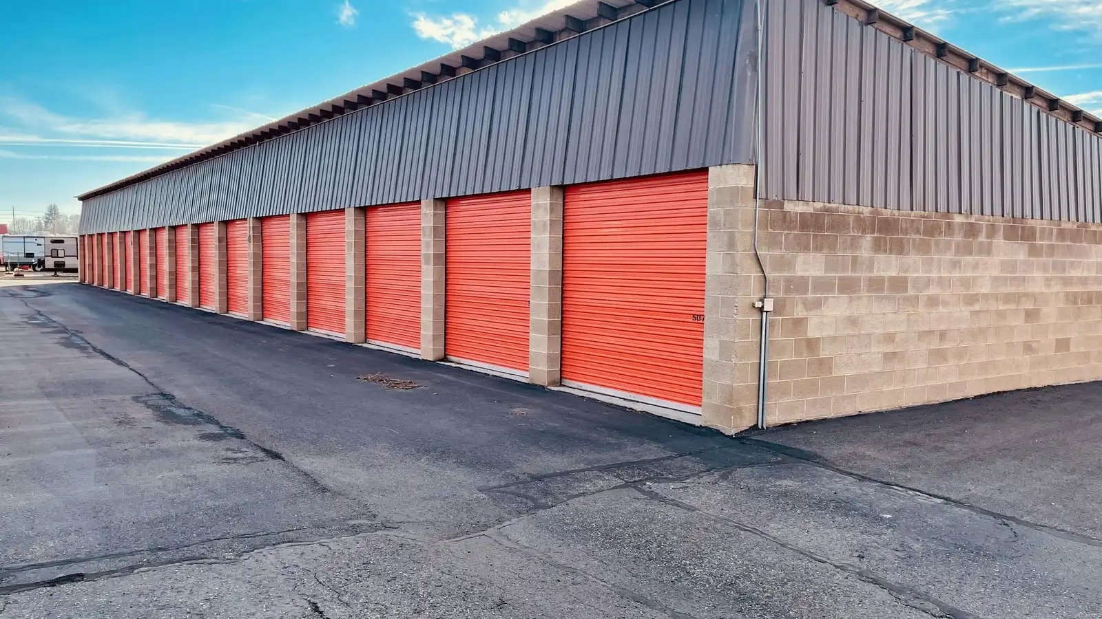 Row of self-storage units with red roll-up doors under a clear sky